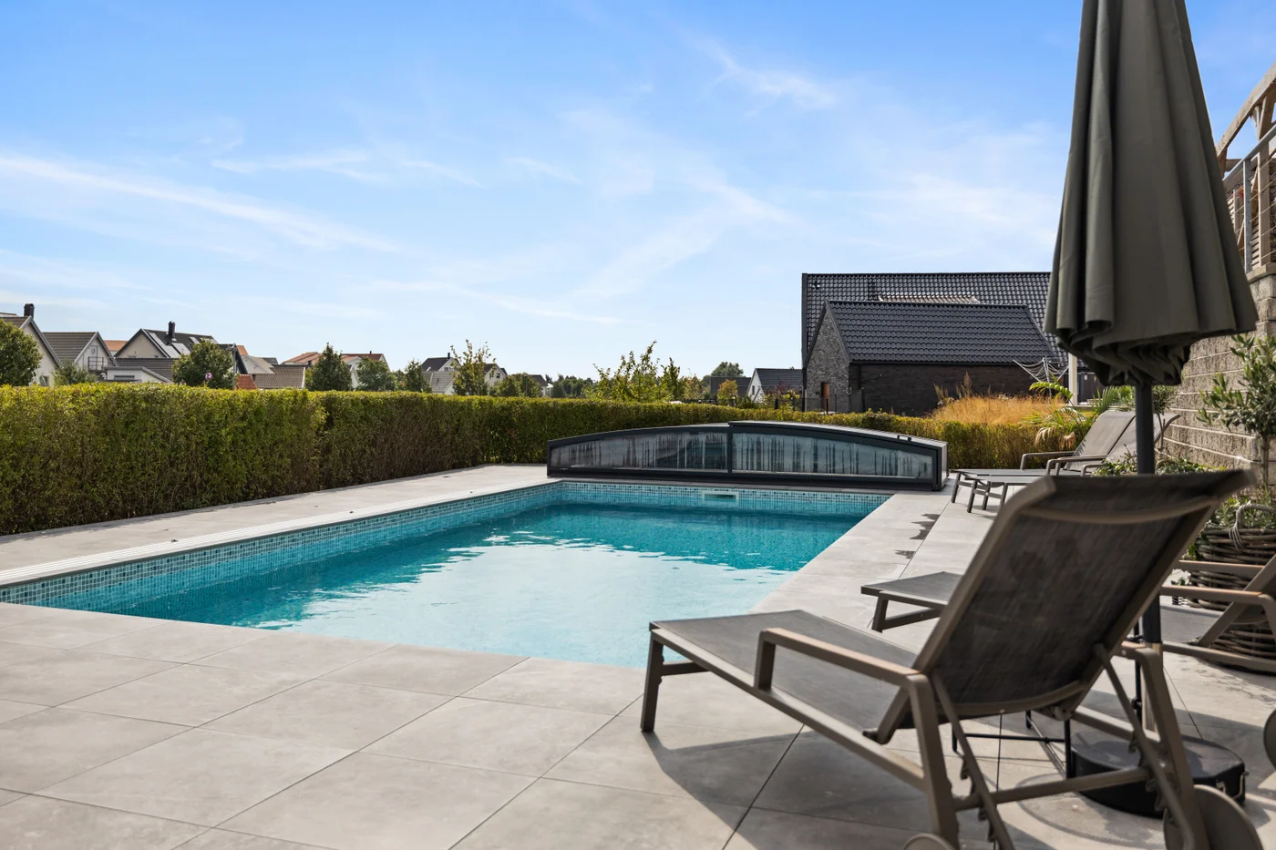 Rektangulär pool med mosaik, pooltak och solstolar i trädgårdsmiljö från kundcase hos Österlens Poolcenter.