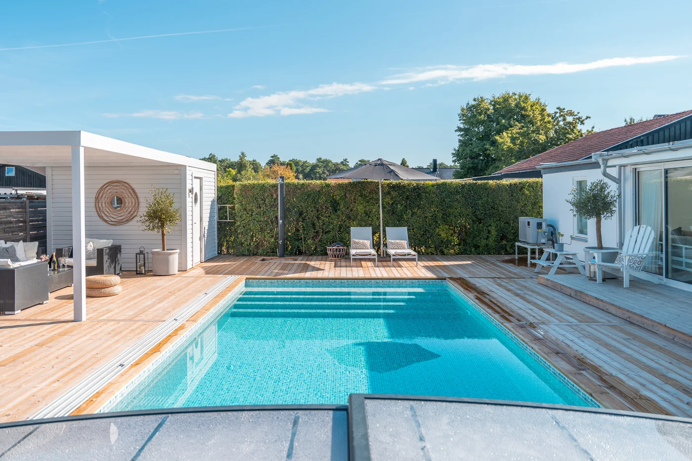 Pool i trädgård med trädäck, loungedel och insynsskydd.